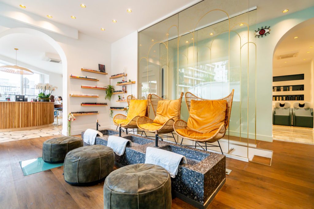 Elegant, helder interieur van een schoonheidssalon met een speciaal pedicurestation met drie mosterdgele rotan fauteuils, stenen wasbakken met witte handdoeken en bijpassende grijze voetenbankjes op een houten vloer.