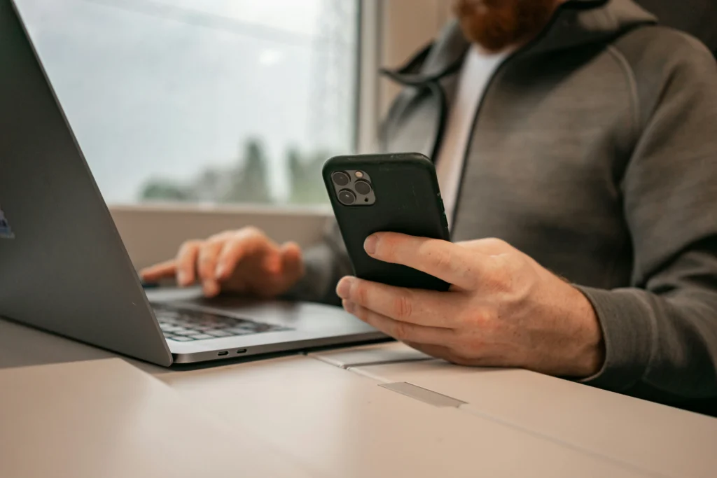 Een saloneigenaar beheert online boekingen op zijn telefoon terwijl hij een laptop gebruikt
